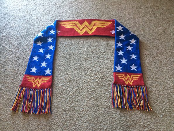 A long scarf with tassled ends. On one side is the Wonder Woman logo against a red backdrop. The other side is blue with white stars.