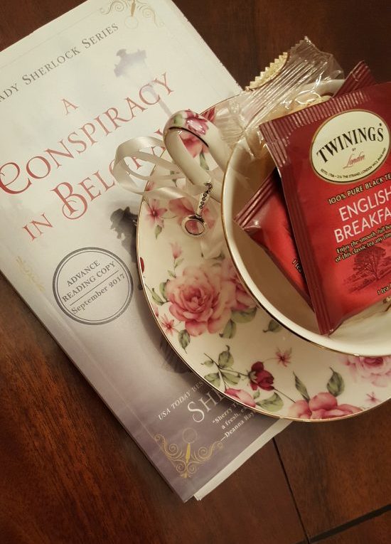 A rose printed teacup with a paper ARC of A Conspiracy in Belgravia by Sherry Thomas