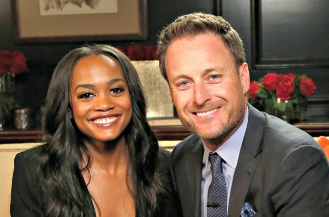 Rachel and Chris Harrison sit on a couch and smile for the camera. Chris looks flush with the blood of innocents.