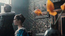 Waltz and Vikander sitting for their portrait, with tulips in a vase in the foreground. A petal falls, because tulips don't last long. Tulips, man.