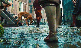 Dane DeHaan walking through the streets of Amsterdam, carrying his painting supplies. The street is muddy and wet.