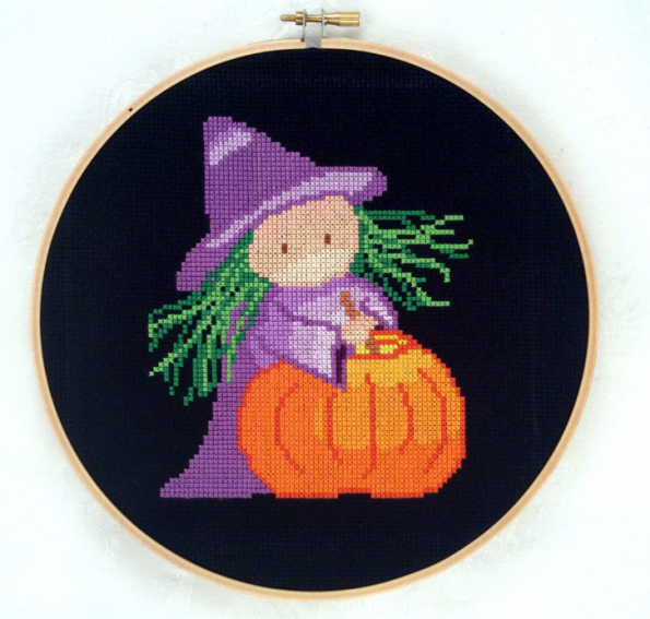 Small witch with green hair in a purple gownin front of a pumpkin