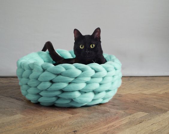 A black cat chills out in a circular cat bed made of giant yarn.