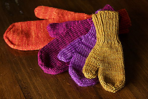 Four mittens in different sizes and colors are displayed on a wooden table.