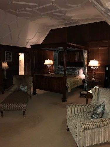 HeatherT's room, featuring a canopy bed, dark wood paneled walls, a white vaulted ceiling, and fuzzy overstuffed striped arm chairs in cream and silver with silver accent pillows
