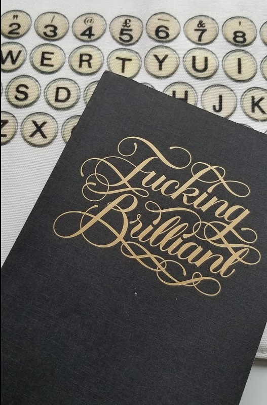 Black paper journal with fucking Brilliant written in script in gold on the cover
