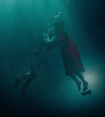 Elisa and Amphibian Man, floating in blue-green water. She is wearing a red coat, and one of her shoes has fallen off her foot.