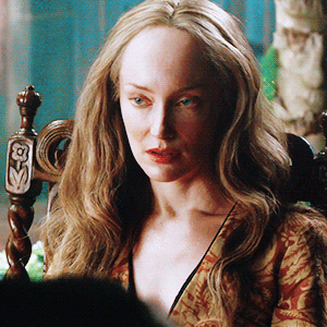 Geillis, sighing and rolling her eyes, wearing a gorgeous gold and red brocade robe.