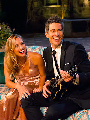 Arie and Kendall sit on the couch. Arie holds a ukulele. 