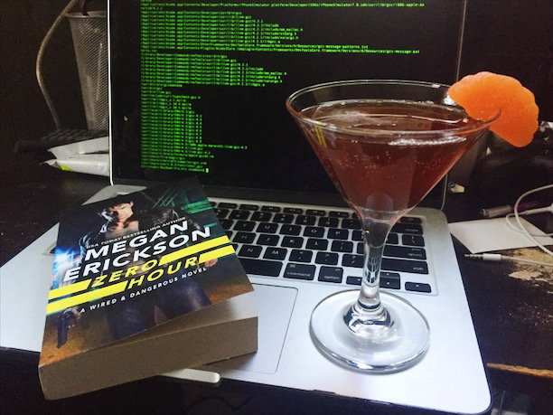 A copy of Zero Hour in front of a laptop screen with code on it. There's a martin glass with an orange colored liquid inside.