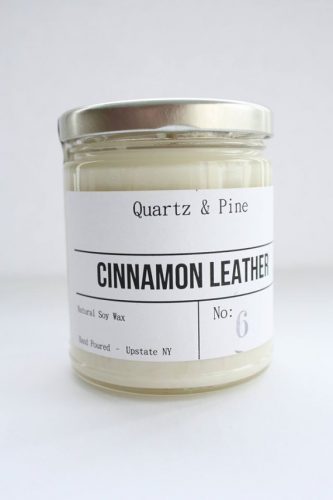 A white soy candle in a jar with the label of cinnamon leather
