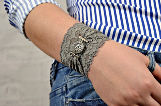 A grey lace stretchy wrist cuff with a grey lace bracelet on top gathered by a buckle charm