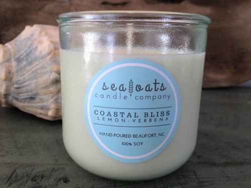 An open glass jar with an off white candle inside and shells displayed in the background