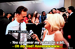 Tom Hiddleston giving his jacket to an interviewer on the red carpet wearing a sleeveless gown and admitting that she is freezing cold