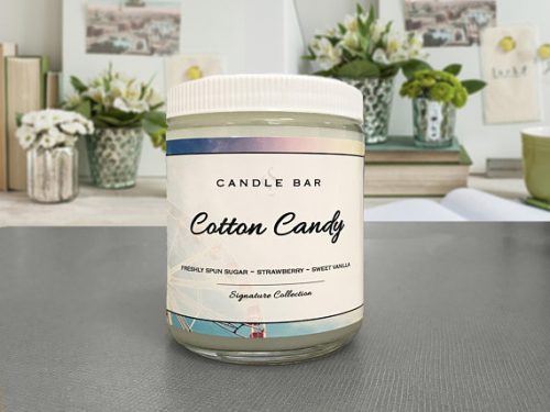The Candle Bar Shop in Cotton Candy scent. A white candle in a glass jar with a rainbow colored label.