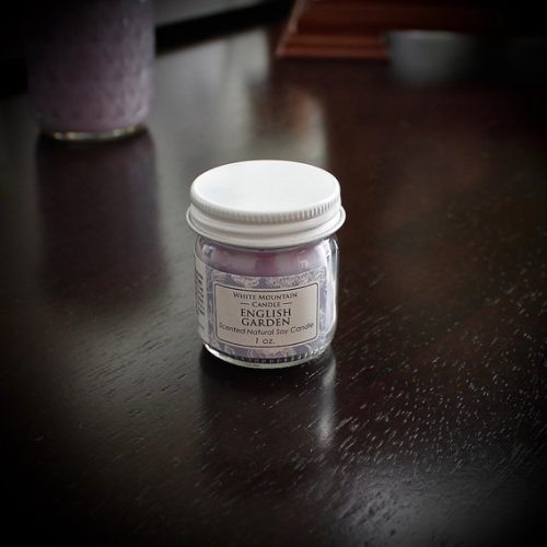 White Mountain Candle in the English Garden scent. A light purple candle on a dark wooden table.