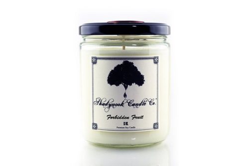 A white candle in a clear jar with a black lid. The candle is sitting in front of a white background and the label has a silhouette of a tree.