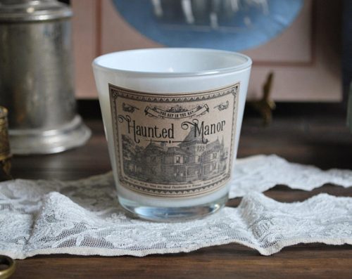 A candle in a frosted glass jar. The label looks aged and yellowed with an illustration of an old manor printed on it.