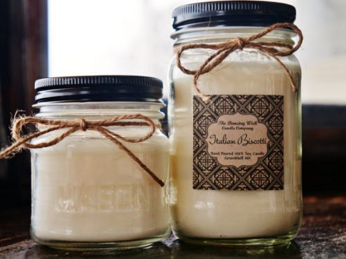 An off white candle in a glass jar with a black lid. The label is filigreed and the lid is decorated with a twine bow.