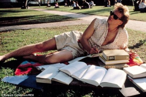 Val Kilmer lounging on grass surrounded by books with his shirt open halfway plus there is a LOT of mullet