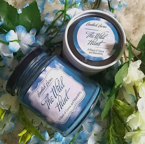 A glittery blue candle in a clear glass jar. The candle is positioned against a backdrop of blue and white flowers.