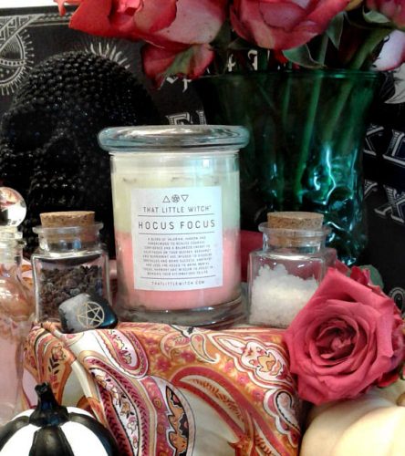 A large glass jar with a white and pink candle inside. The candle is surrounded by pink flowers and apothecary jars. 