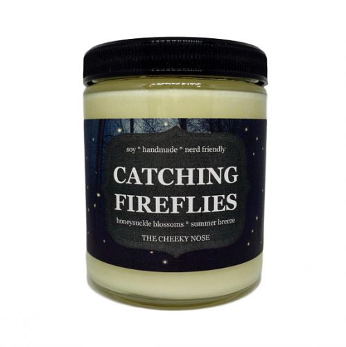 An off white candle in a jar with a glass lid. The label is dark blue with the silhouette of a forest with little fireflies.