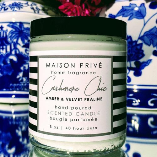 A white candle in a clear jar with a black lid. The label has black and white stripes and the text is in flowing script.