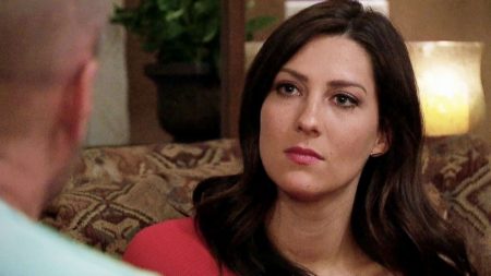 Becca sits on a couch and looks at a man who is off screen