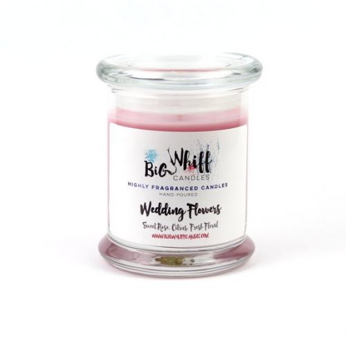 A pink candle in a glass jar with a lid. The label has swirly, wispy text and some watercolor strokes.