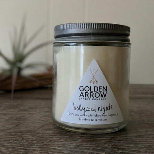 An off white candle in a glass jar with a metal lid on a wooden table.