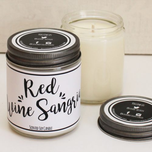 A white candle in a glass jar with a metal lid. The label is white with black swirly text.