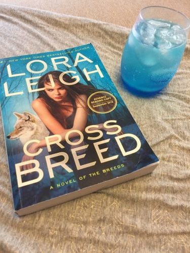 A bright blue drink in a clear glass next to a copy of Cross Breed.