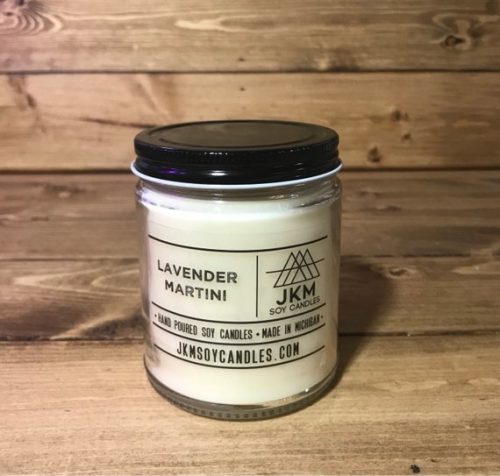 A white candle in a glass jar displayed in front of a washed wood background.