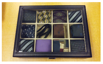 Neckties and bowties in a case from the NYPL available for lending against a woodgrain tabletop
