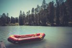 Inflatable boat on water on the river or lake near the shore in a clear summer day, the bright reflections on the waves. Red boat at the wooden bridge in the blue lake. fishing boat. rescue boat.