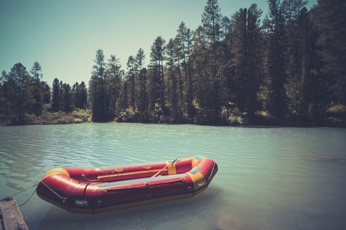 Inflatable boat on water on the river or lake near the shore in a clear summer day, the bright reflections on the waves. Red boat at the wooden bridge in the blue lake. fishing boat. rescue boat.