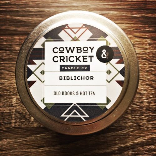 A white candle in a metal tin with a geometric black and white label.