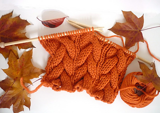 The start of an orange cabled scarf on wooden straight needles is featured with leaves in the background.