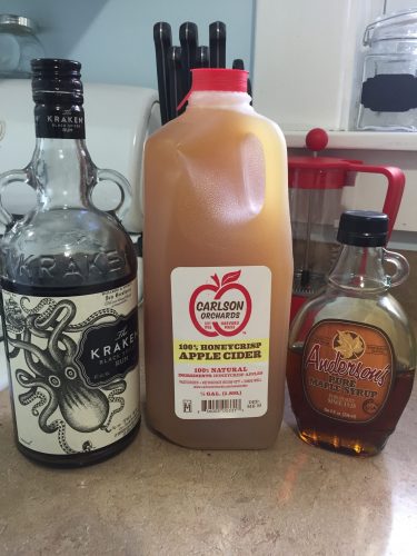 A bottle of Kraken rum, a jug of cider, and a glass jar of maple syrup on a kitchen counter.