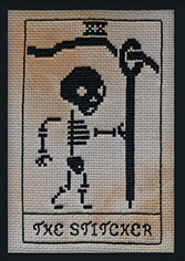 Black cross stitch of a skeleton holding a large tapestry needle with The Stitcher in text beneath 