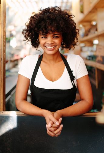 Woman barista inside her coffee shop. Curly haired woman standing behind the counter of a coffee shop.