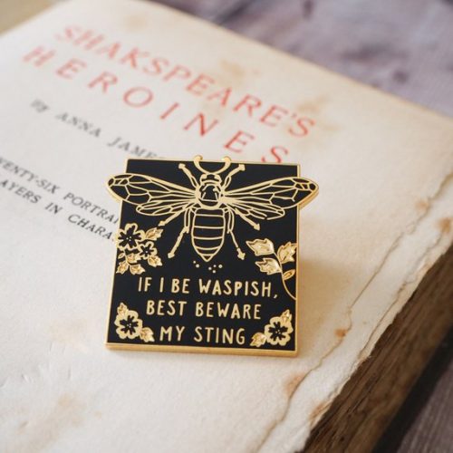 A black and gold enamel pin of a wasp that reads if I be waspish best beware my sting.