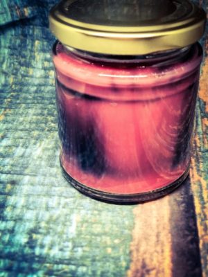 A burnt red candle in a glass jar with a yellow metal lid.