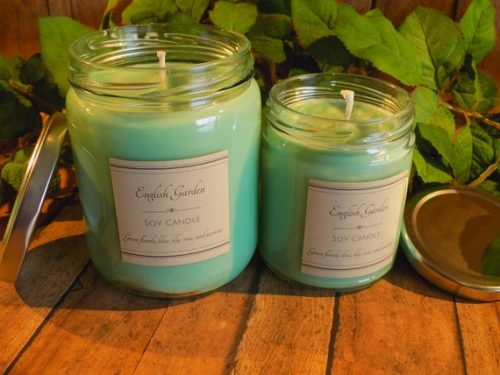 Two differently sized light green candles on a warm, wooden table. Behind the candles are green vines of ivy.