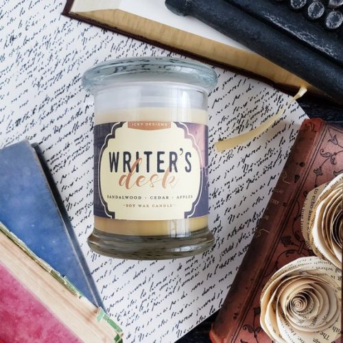 A tan candle in a glass jar. It's rest on a handwritten letter, surrounded by books.