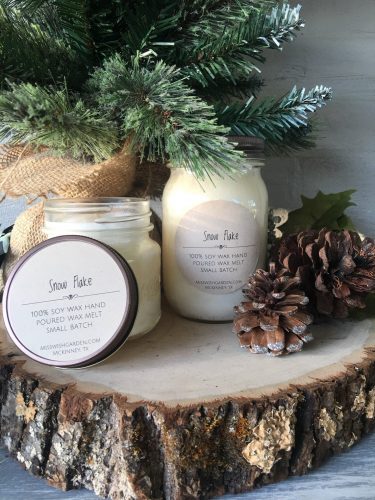 One tall candle and one short candle in glass mason jars. They're sitting on a stump surrounded by pine needles and pinecones. 