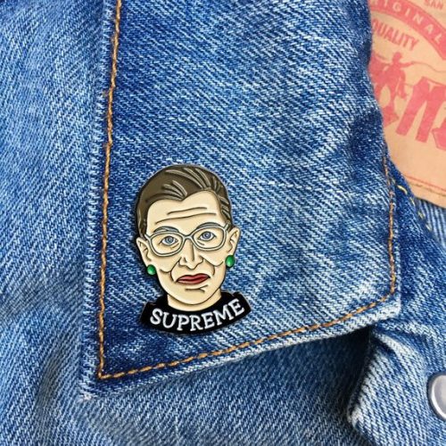 An enamel pin of Ruth Bader Ginsberg with the words supreme.