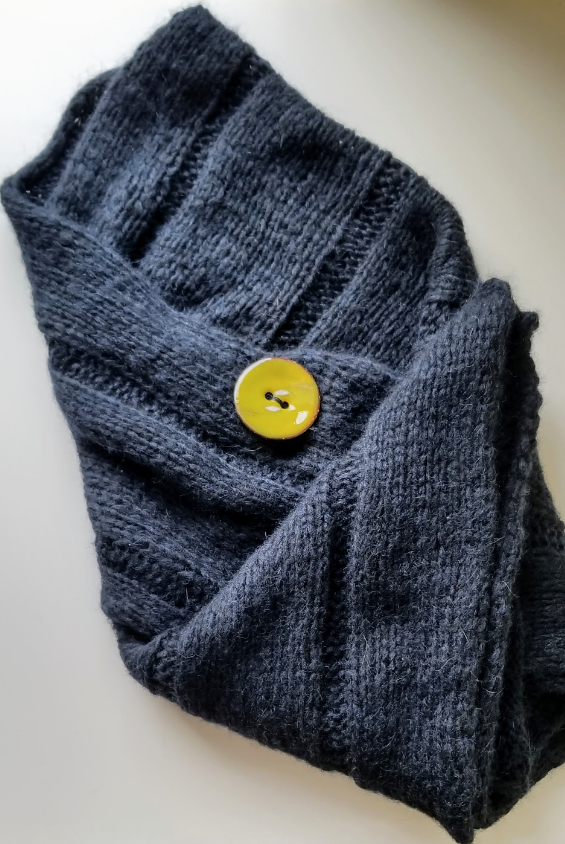 Deep blue knit shawl folded on a white background with a large yellow enamel button