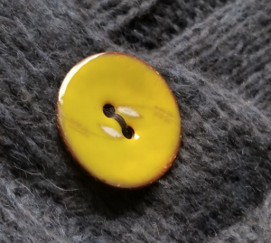 Close up of gold-yellow enamel button with two pieces of wheat that nearly connect over the buttonholes